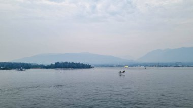 Bu görüntü Victoria Limanı 'nın, Vancouver Adası' nın, uzaktaki görkemli dağların ve oradan geçen bir uçağın manzarasını gösteriyor. Huzurlu manzara huzur ve doğal güzelliği çağrıştırıyor..
