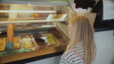 Küçük bir kız bir dondurma dükkanının önünde duruyor. Yüksek kalite 4k görüntü