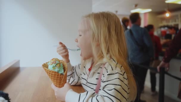 4歳の女の子がカフェでアイスクリームを食べています 通りからガラス越しに眺めます 高品質4K映像 — ストック動画