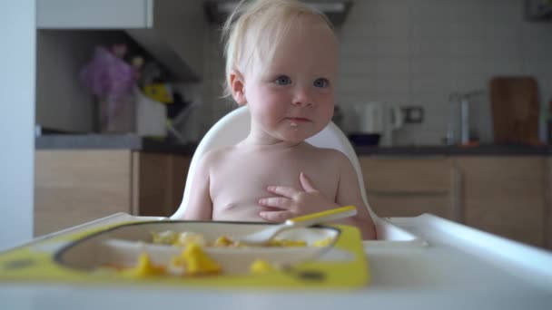 面白い女の子の赤ちゃんは 子供のための優しい庭の健康的な食事の栄養で高給餌椅子で彼女自身の笑顔の幼児の赤ちゃんによって食べる彼女の手で食べる — ストック動画
