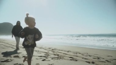 2021 Alanya. Hindi. Sevimli küçük bir kız anne neşeyle deniz boyunca koşuyor, gülüyor. Annelik, annelik, bekar anne, aile kavramı. Yavaş çekim 120