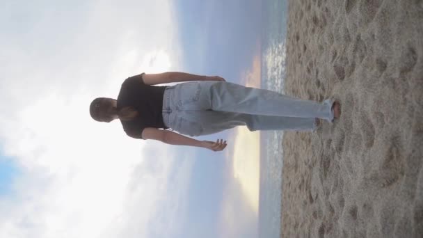 Вертикальное Видео Молодая Женщина Легких Джинсах Идет Закатному Морю Песке — стоковое видео