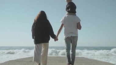 İskelenin sonuna doğru yürüyen dört kişilik genç bir aile. Gerçek bir aile. Sevgi. Denizde bir sabah. Güneşli bir aralık. Ağır çekim 120 Yüksek kalite FullHD görüntü Alanya Türkiye 2021