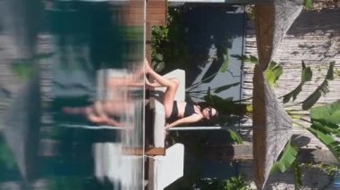 Dikey video hikayeleri. Havuz kenarında güneşlenen güzel bir kadın. Mavi havuz suyu ve sıcak hava. 4k Alanya. Türkiye 2021 
