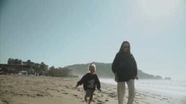 2021 Alanya. Hindi. Sevimli küçük bir kız anne deniz boyunca neşeyle koşuyor, sahilde yürüyor, gülüyor. Annelik, annelik, bekar anne, aile kavramı. Yavaş çekim