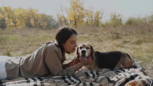 少女は芝生の芝生の上に横たわり ビーグル犬を抱きかかえ 彼に優しくキスをしている 秋のコンセプト 犬は人間の親友であり 動物への愛です キエフ ウクライナ2019 — ストック動画