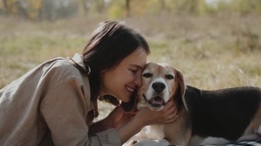 Bir kız çimenli bir çimenlikte uzanır, av köpeğine sarılır ve onu nazikçe öper. Ağır çekim. Köpek insanın en iyi dostudur, hayvanları sever. Kyiv. Ukrayna. Yavaş çekim 120