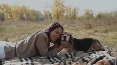 Çimenlerde yatan, av köpeğine sarılan ve gülümseyen bir kız. Köpek insanın en iyi dostudur, hayvanları sever. Ağır çekim 120. Sonbahar