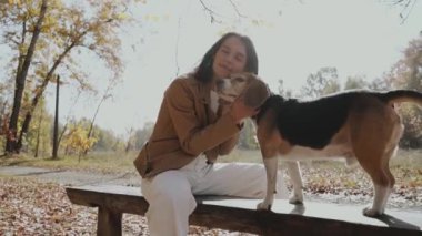 Parktaki bankta köpeğiyle oturan bir kız. O, nazikçe köpeğine sarılıyor. Autumn, Köpek insanın en iyi dostudur, hayvanları sever. Yavaş Hareket