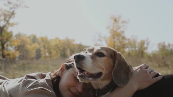 芝生の芝生の上に女の子のラウンジ 彼女のビーグル犬と抱き合って 彼女は喜んで目を閉じている コンセプト 犬は人間の親友 動物への愛です スローモーションショット120 — ストック動画