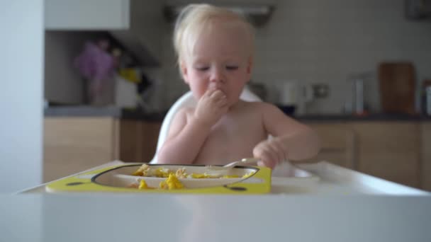 かわいい赤ちゃん人形が皿の上にフォークをドラミングします 台所に座りなさい 優しい庭の高い給餌椅子の赤ちゃん子供のための健康的な食事の栄養 — ストック動画