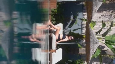 Dikey video hikayeleri. Havuz kenarında güneşlenen güzel bir kadın. Mavi havuz suyu ve sıcak hava. 4k Alanya. Türkiye 2021 