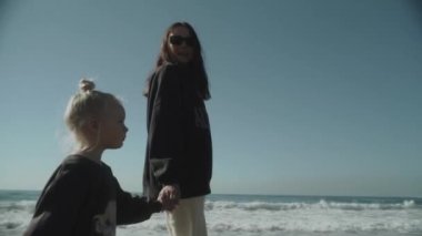 Küçük bir kız annesinin elini tutuyor. Onlar bir mağara sahilinde deniz boyunca yürüyorlar. Yavaş hareket eden annelik, annelik, bekar anne, aile kavramı. Alanya Türkiye 2021