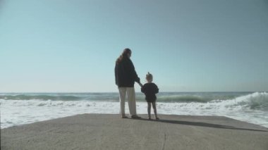 Bir anne ve tatlı küçük kızı rıhtımda durur ve denizin fırtınalı dalgalarını seyrederler. Ağır çekim 120 Yüksek kalite FullHD görüntü