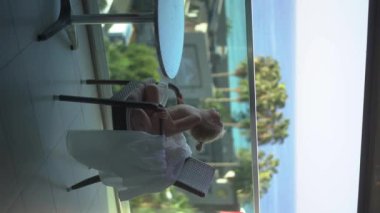 Dikey video. Makaralar. Hikayeler. Şirin küçük bir kız, açık hava otel odasının balkonunda deniz manzaralı bir yerde kahvaltı yapıyor. Mükemmel Günaydın. Alanya Türkiye 2021 Yüksek kaliteli 4K görüntü