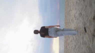 Dikey video hikayeleri, sahilde tek başına dans eden genç bir kadını çekiyor. Olumlu duygular. Özgür yaşam tarzı Tek başına