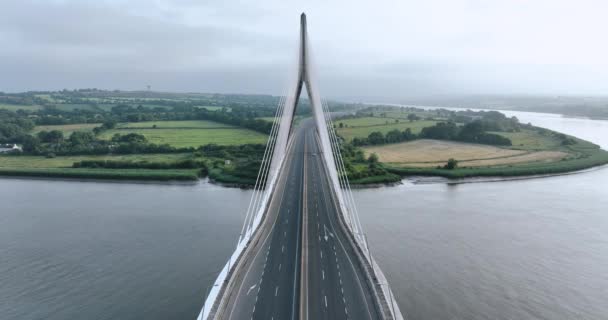 两辆汽车穿过桥向摄像机驶去 后面是一座绿色岛屿上的斜拉桥 爱尔兰沃特福德斯韦尔河上的斜拉桥4K — 图库视频影像