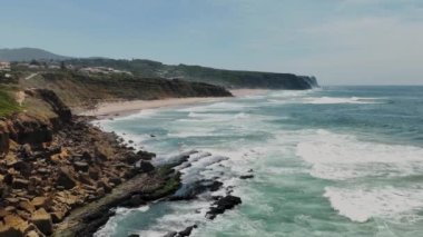Yavaş çekim 4K. Portekiz, Sintra 'da beyaz dalgaları olan Atlantik Okyanusu kıyısında engebeli bir uçurum. Sintra Praia das Macas. 