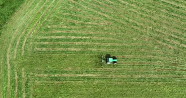 Havadan. Yeşil bir traktör yeşil bir çayırdan geçiyor ve çimleri kesiyor. Kamera arkasında hareket ediyor. Yüksek kalite atış 5 bin.