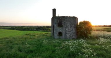 Havadan. Dairesel. Eski bir tapınağın kalıntıları, Kilkenny yakınlarındaki İrlanda 'nın yeşil tarlalarına karşı bir dağın tepesinde duruyor. Güneş harabelerden geçip 5k odasına doğru parlıyor.
