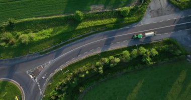 Hava görüntüsü. Yeşil tarlalara karşı bir yolda geçen traktörün yukarıdan görünüşü. İrlanda 2023 yüksek kaliteli 5k görüntü