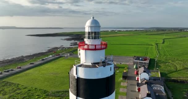エアリアル4K 緑地と干し草の海を背景にした巨大な灯台 アイルランドのウェックスフォード郡のフック半島 世界最古の灯台は12世紀に建てられました — ストック動画
