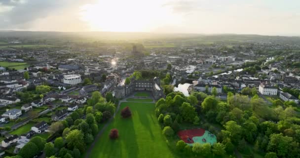 アリアル アイルランドの緑豊かな公園を通ってキルケニー城へのフライト 川ノアと夕日を背景に 古代の町 5K形式の高品質のショット — ストック動画