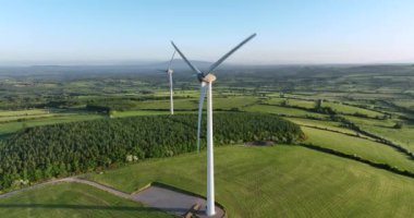 Yeşil tarlalara karşı bıçakları olan büyük bir rüzgar türbini. Ireland 'ın yeşil vadisinin havadan görünüşü. Alternatif enerji. İrlanda. Yüksek kalite 4k görüntü
