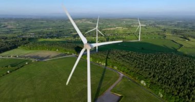 Yükseltilmiş bir bölgedeki güzel mavi gökyüzünde enerji üretimi için bir yel değirmeni çiftliğinin havadan görünüşü. Sürdürülebilir kalkınma için temiz yenilenebilir enerji üreten rüzgar türbinleri 4k