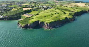 Havadan. Uçup gidiyoruz. Okyanusun yakınındaki kayalık kayalıklarda bir golf sahası. Dunmore East County Waterford, İrlanda 'da. Yüksek kalite 4k görüntü