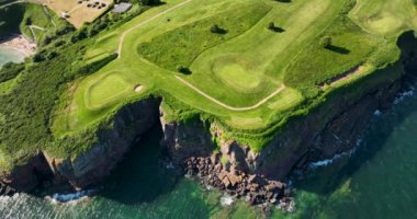 Havadan. Uçup gidiyoruz. Okyanusun yakınındaki kayalık kayalıklarda bir golf sahası. Dunmore East County Waterford, İrlanda 'da. Yüksek kalite 4k görüntü