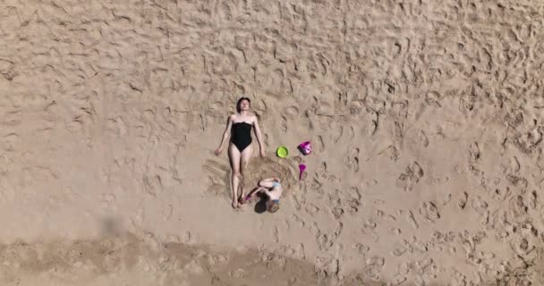 エアリアル 母親と子供はビーチでリラックスしています 母親は日光浴をしていて 子供は母親を砂浜で過ごしています ポルトランド 海によって休日 5Kについて — ストック動画
