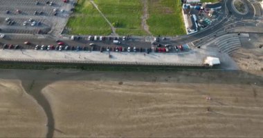 Havadan. Dikey. Okyanus sahili dalgalarla yıkar. İnsanlar gün batımında sahilde yürüyorlar. Sahil boyunca park etmiş arabalar. Tramore, Waterford 'dan. İrlanda 4k