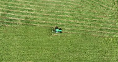 Hava fotoğrafçılığı. Yeşil bir traktör yeşil bir çayırdan geçiyor ve çimleri kesiyor. Kamera arkasında hareket ediyor. Yüksek kalite atış 5 bin.