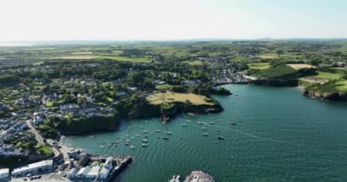 Hava 4k. Kayalık kıyı şeridinde balıkçı tekneleri olan güzel bir deniz feneri. Gün batımı. Dunmore East County Waterford, İrlanda.