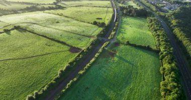 Havadan. Hızlı bir tren gün doğumunda pitoresk yeşil bir tarlanın önünden geçer. Tren küçük bir köprünün altından geçer. Blarney Cork İrlanda 4k