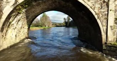 Havadan. Inistigoe County Kilkenny İrlanda 'daki Nore nehrinin üzerinde 18. yüzyıldan kalma bir köprünün altından bir dron uçuyor. İrlanda 'da bir nehre karşı eski bir taş köprü. Yüksek kalite 4k görüntü