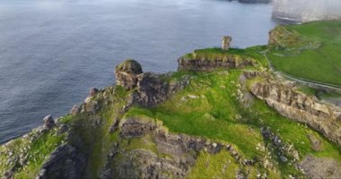 Hava 4k. Kamera, tel örgülü kayalıkların üstündeki taş kulenin üzerinden uçuyor. Okyanus dalgaları kayalık kıyıları ve taş oluşumlarıyla kayalıklara çarpıyor. Yüksek kalite 4k görüntü