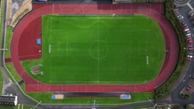 Bir olimpiyat ve futbol stadyumunun yukarıdan aşağıya bakan hava aracı görüntüsü. Büyük bir stadyum, koşu pisti ve geniş bir saha. Stadyumun yanındaki otoparkta arabalar var. Yüksek kalite 4k görüntü