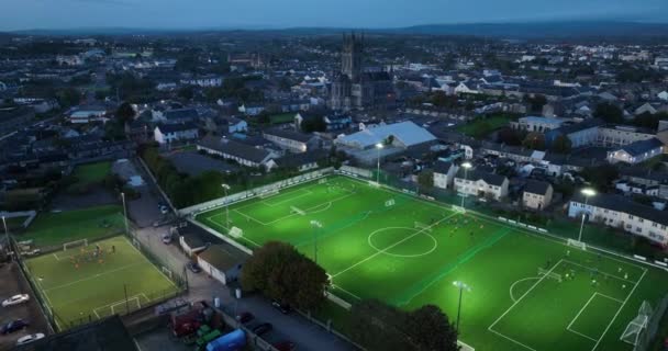 足球场的空中夜景 绿绿的足球场映衬着古城和大教堂的背景 球员在晚上踢足球和训练 明亮的体育场 秋季4K镜头 — 图库视频影像