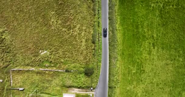 在阳光明媚的早晨 一辆汽车沿着空旷的石子路驶过绿茵的草地 没人追着车一辆黑色汽车沿着绿地行驶 高质量的4K镜头 — 图库视频影像