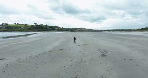 一个女人走在荒芜的海滩上 孤独和寒冷 一个荒芜的海滩一个关于海洋的观点 桑迪海滩蓝水 多云的天气 英奇多尼海滩 高质量的4K镜头 — 图库视频影像