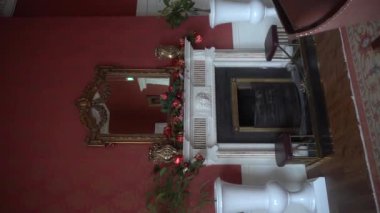 Dikey. Şöminenin üstündeki Noel süsleri, Noel ağacı ve şömineyi süsleyen kırmızı süslemeli bir çelenk. Peri masallarındaki dayanılmaz bir Noel ağacı. Vintage iç mimari