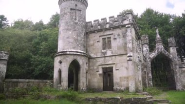 Ballysaggartmore Kuleleri. İrlanda 'da yeşil bir ormanın arka planına karşı antik bir kapı. Mistik İrlanda. Lismore İlçesi Waterfords Ormanı 'ndaki ortaçağ köprüsünden geçen bir kamera. Bir mistik