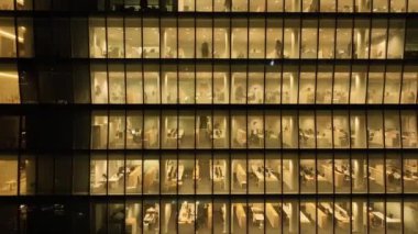 Havadan. Camdan bir gökdelenin ofis pencerelerinden sinematik bir görüntü. İş adamları geç saatlere kadar çalışıyor. Bir gökdelenin penceresinin yakınındaki bir dronun panoraması. Yüksek