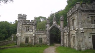 Ballysaggartmore Kuleleri. İrlanda 'da yeşil bir ormanın arka planına karşı antik bir kapı. Mistik İrlanda. Lismore İlçesi Waterfords Ormanı 'ndaki ortaçağ köprüsünden geçen bir kamera. Bir mistik