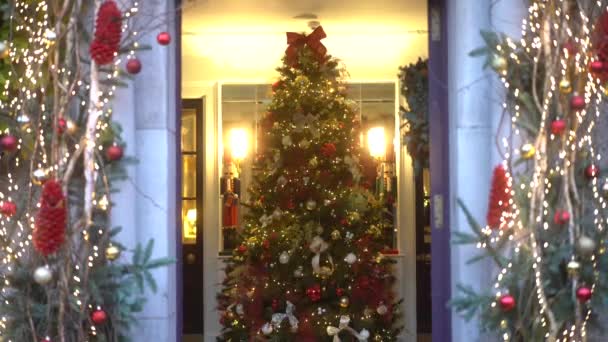家の入口のクリスマスと新年の木 クリスマスと新年のインテリアデコレーション おもちゃ ギフト 現在の箱 点滅するガーランド 照らされたランプで飾られる緑の木 コージー — ストック動画