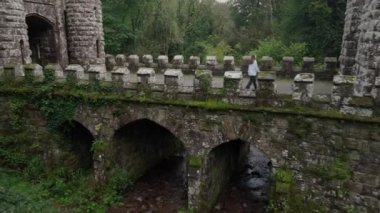 Ireland 'ın Ballysaggartmore Kulelerinin insansız hava aracı görüntüsü. Lismore İlçesi Waterfords Ormanı 'ndaki ortaçağ köprüsünde tek başına yürüyor. Mistik bir mekan. Ortaçağ binası. Kaleye açılan kapı.