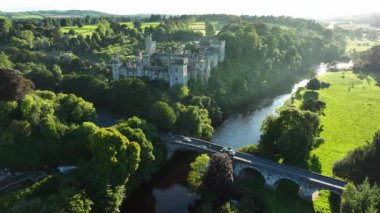 Gün batımında yeşil ağaçlara sarılmış nehrin kıyısındaki inanılmaz şato. Akşam güneşi Castle. Lismore Kalesi ve Knockmealdown Dağları Waterford Ireland 'ın verimli kırsalında Antik Doğu' da. Lismore