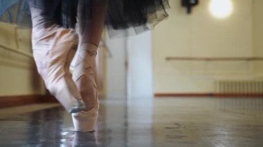 Karanlık sahnede ya da stüdyoda egzersiz yaparken bale dansçılarını yakın çekim yapın. Sivri uçlu bir balerin yerde dans ediyor. Dansçılar bacaklarını kapatır. Salonda bale eğitimi. Kadın ayağı.